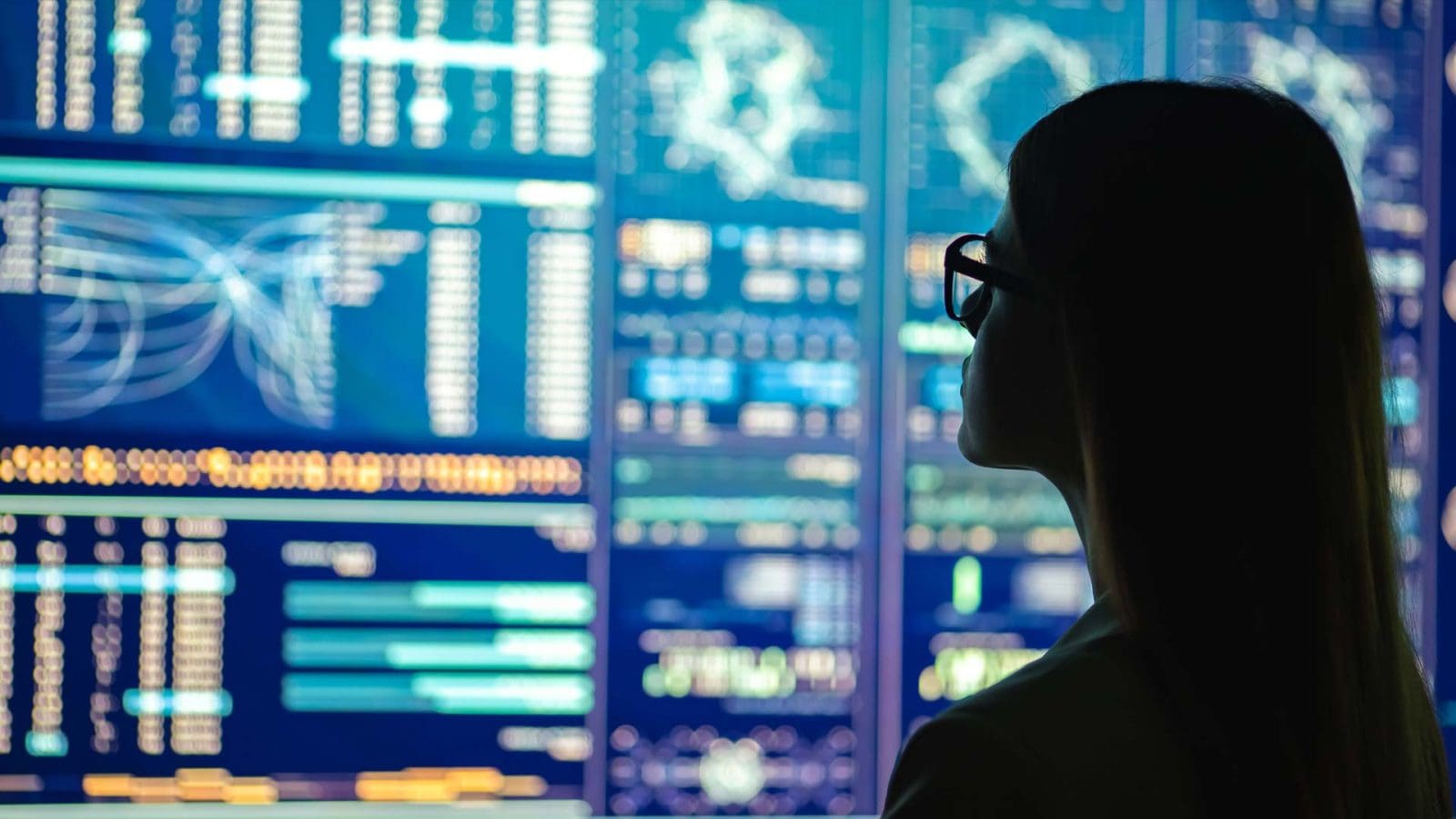 A silhouette of a person studying screens of data